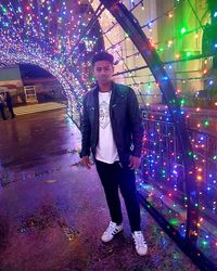 Full length portrait of young man standing against illuminated lights at night