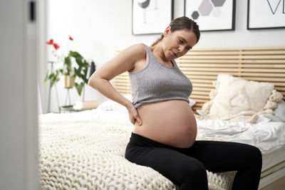 Pregnant woman sitting on bed at home