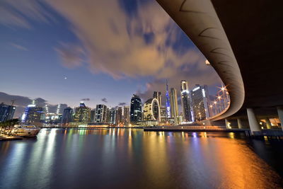 Illuminated bridge over river and buildings against sky at night