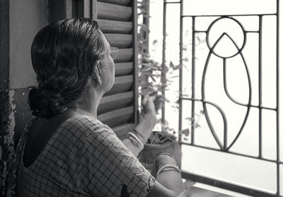 An aged bengali woman taking care of potted houseplant standing near window