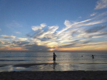 Silhouette people in sea against sky during sunset