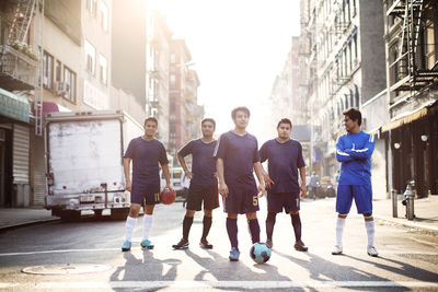 Confident soccer players standing at city street against clear sky