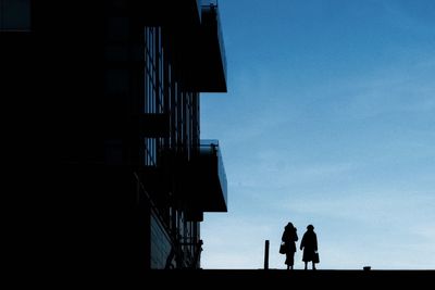 Silhouette people walking by building against sky