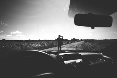 Man photographing car on field against sky