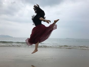 Side view of woman dancing at beach against cloudy sky