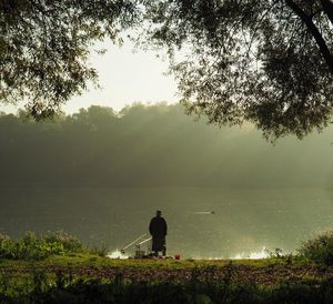 Rear view of man fishing in lake against clear sky