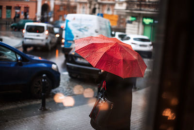 Person with red umbrella standing on sidewalk during rainy season in city