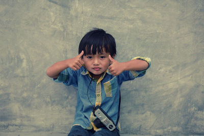 Portrait of boy with camera against wall
