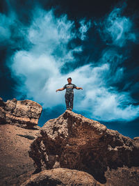 Low angle view of man standing on rock against sky