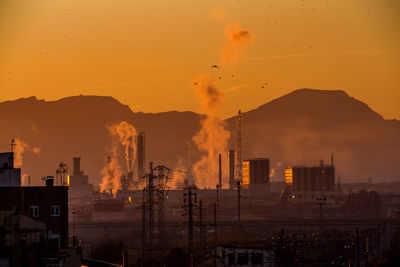 Smoke emitting from factory against sky during sunset