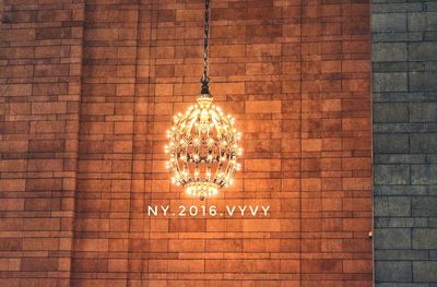 Low angle view of illuminated lamp hanging on brick wall