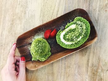 Cropped hand of woman holding plate with matcha cake at wooden table