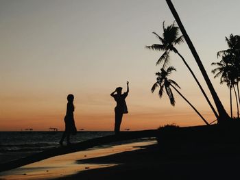 Silhouette people on beach against sky during sunset