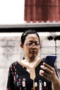 Woman using mobile phone while standing against wall