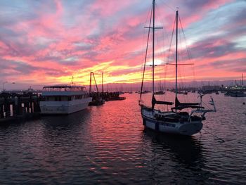 Sailboats moored on sea against sky during sunset