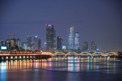 Illuminated buildings by river against sky at night