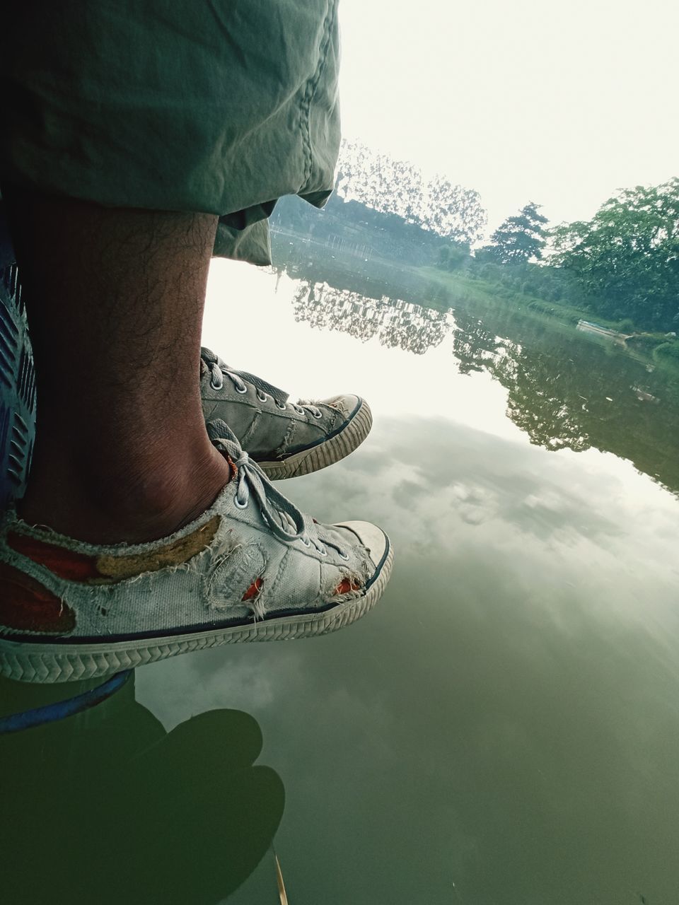 low section, human leg, shoe, one person, water, footwear, limb, human limb, green, nature, adult, day, leisure activity, men, lake, standing, reflection, lifestyles, human foot, outdoors, blue, casual clothing, clothing, relaxation