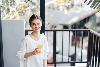 Portrait of young woman standing against railing