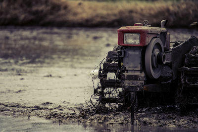 Close-up of abandoned machinery on field by lake