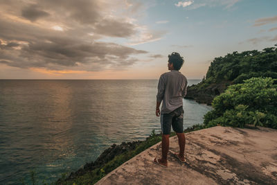 Rear view of man standing by sea against sky during sunset