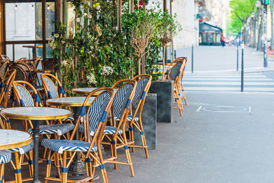 Empty chairs and tables at sidewalk cafe in city