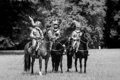 Men riding horses on field against trees