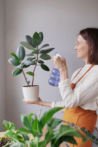 Side view of young woman holding plant