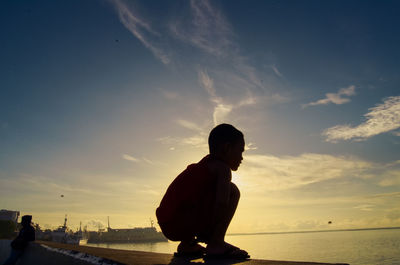 Silhouette boy standing on beach against sky during sunset