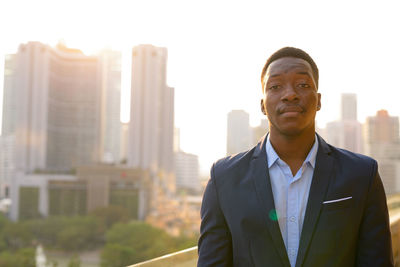 Portrait of young man standing against cityscape