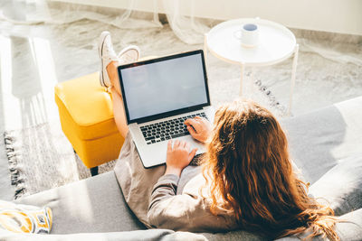 Rear view of woman using digital tablet on bed at home