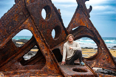 Portrait of man sitting on rusty metal against sky