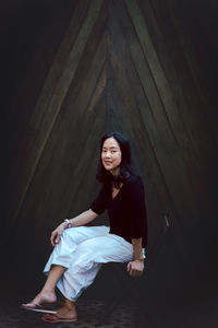 Full body portrait of asian woman sitting on chair on wooden background.