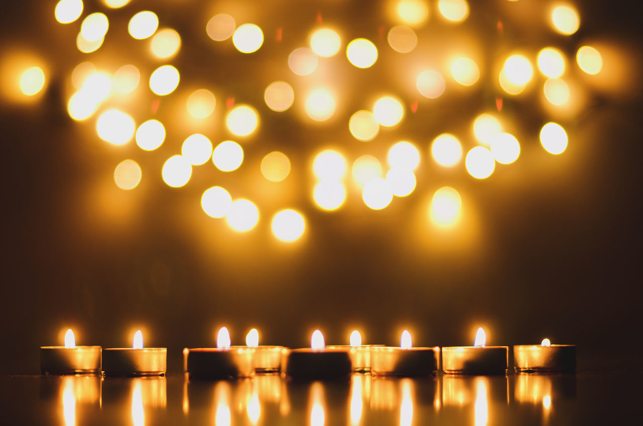 CLOSE-UP OF ILLUMINATED CANDLES AGAINST LIGHTS