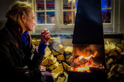 Woman smoking cigarette by bonfire at night