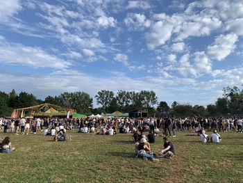 Group of people relaxing on field against sky