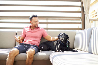 A man relaxes outdoors with a drink and his dog.