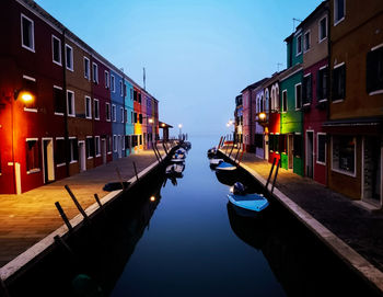 Boats moored in canal amidst buildings against sky in city
