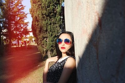 Portrait of young woman wearing sunglasses standing against trees