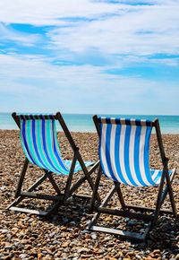 Deck chairs on beach against sky