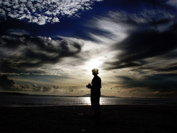 Silhouette man standing on beach against sky during sunset
