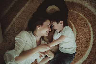 Beautiful brunette mom playing and hugging with her son on the floor in a home-like normal interior