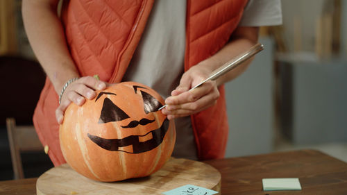 Midsection of man holding jack o lantern on table
