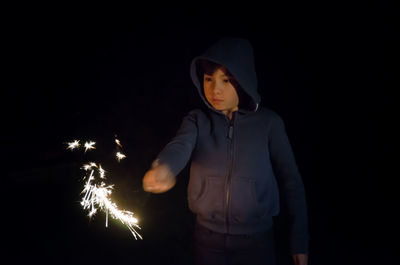 Cute boy holding sparkler while standing over black background