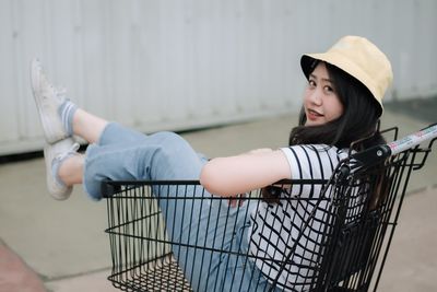 Portrait of smiling young woman sitting in shopping cart