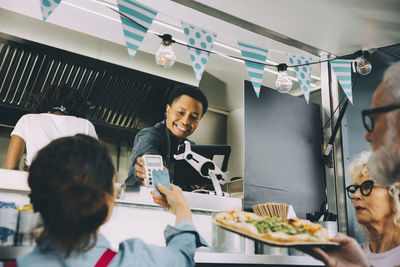 Smiling male owner talking to customer about contactless payment while standing in food truck