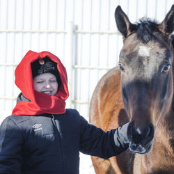 Boy smiling while standing with horse against wall
