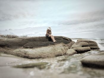 Full length of woman sitting on rock at beach