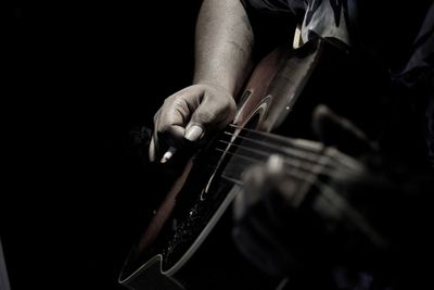 Midsection of man playing guitar over black background