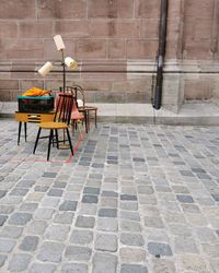 Empty chairs and tables on sidewalk against wall