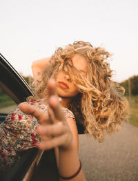 Portrait of young woman holding camera against sky